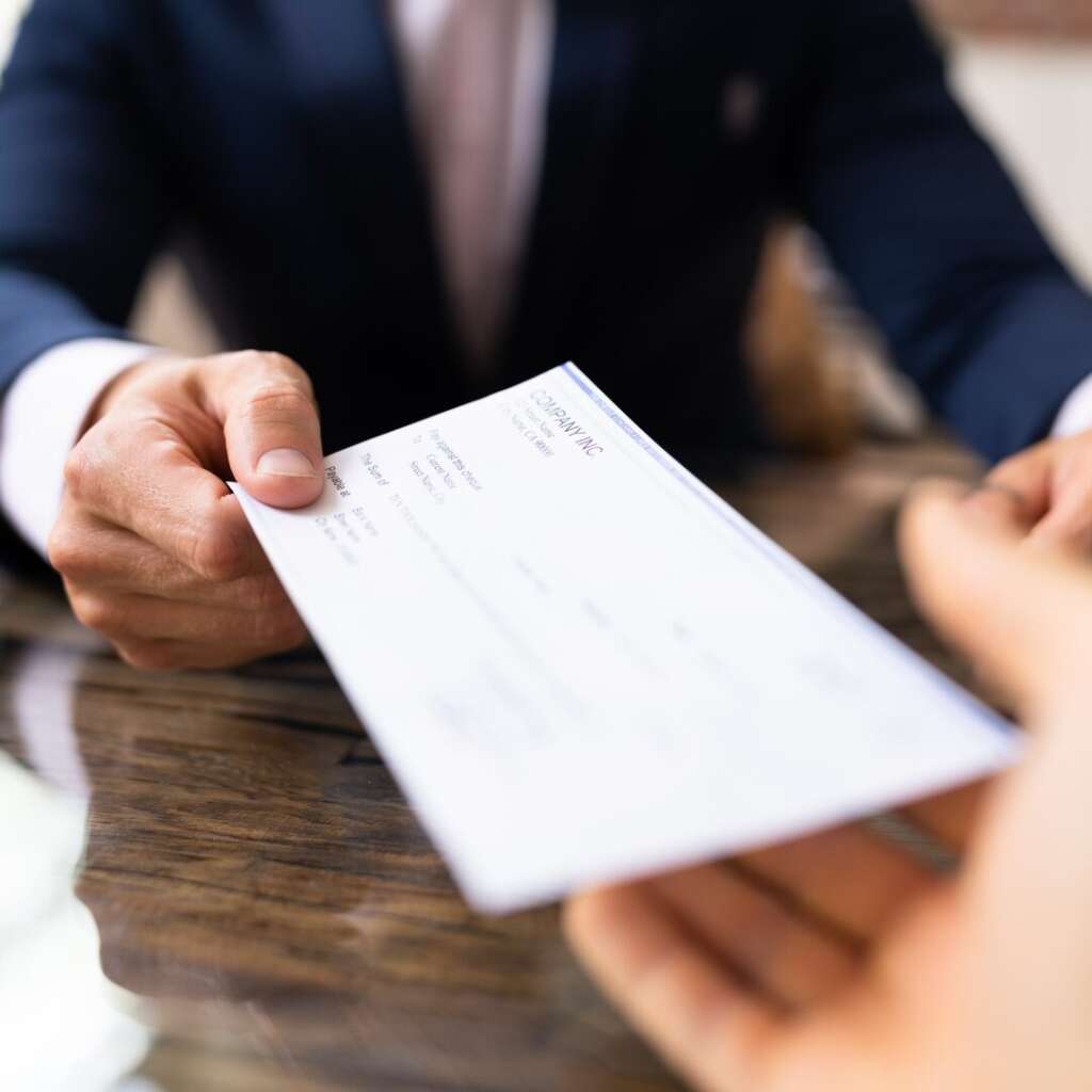Person handing another persona check from their business representing compensation classification. 
